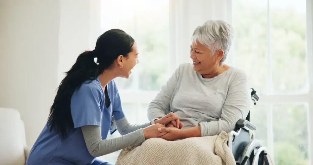 Caregiver holding hands with a smiling senior woman at home